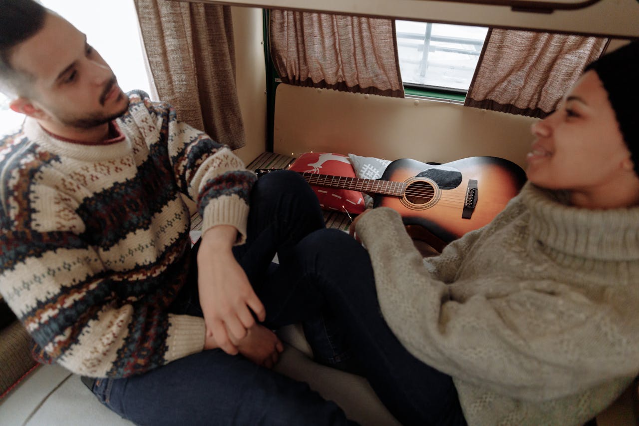 A couple enjoying a cozy moment inside a camper van, with a guitar and warm sweaters.